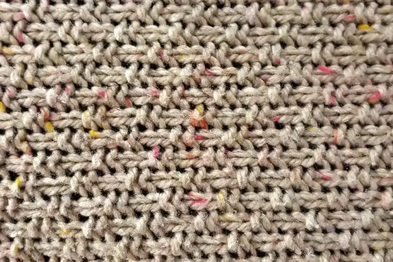 Beige acrylic knit fabric with speckled threads observed in a close-up view