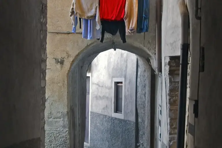 Clothes hung on a line across a narrow alley with an arched stone doorway.