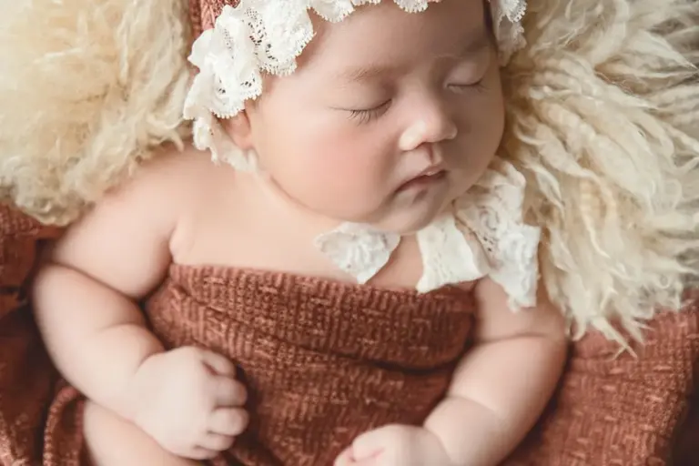 Sleeping baby wrapped in a plush brown blanket with a delicate lace headband.