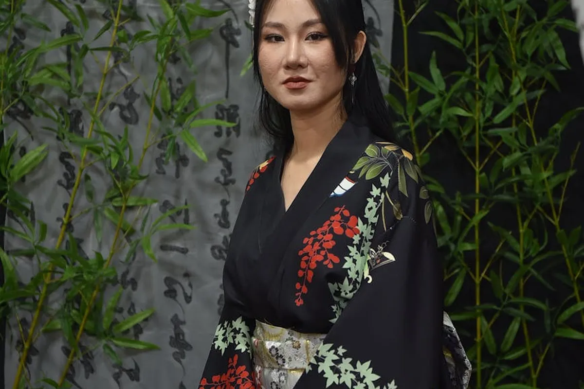 Portrait of a woman in a black floral kimono standing among tall bamboo stalks.