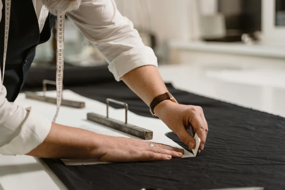 Tailor measuring a piece of dark basketweave shirting fabric on a worktable with a measuring tape