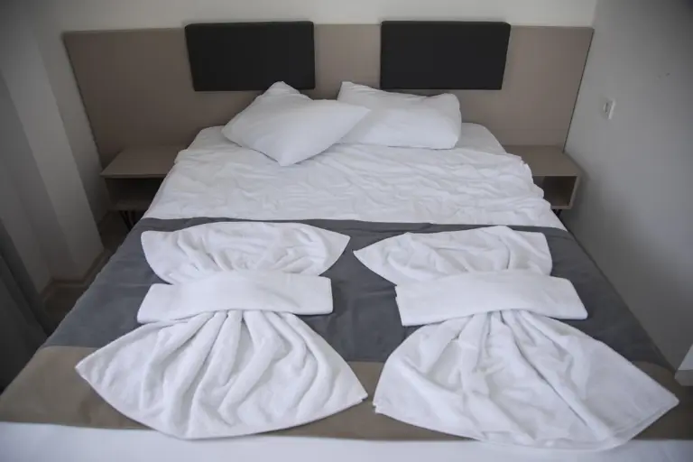 A neatly made bed with white sheets and pillows, and decorative towels folded at the foot of the bed.