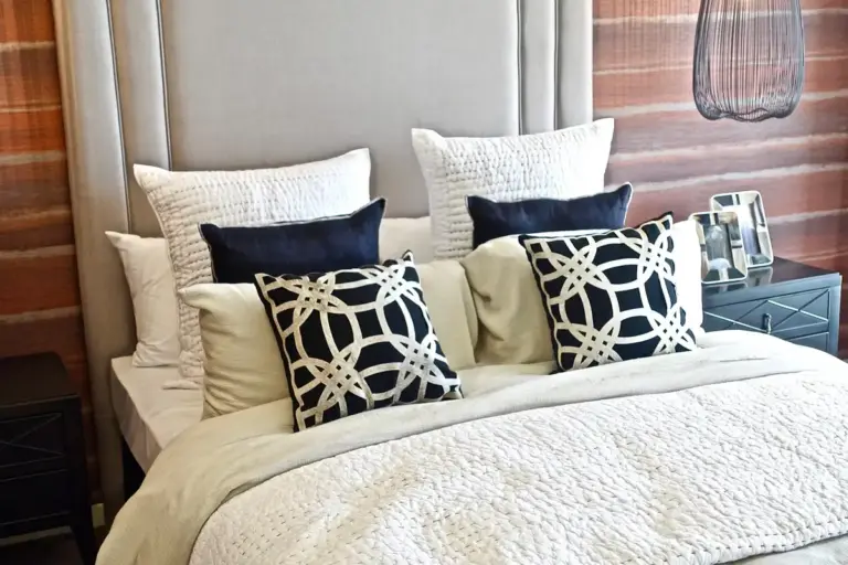 A neatly made bed with white linen bedding and decorative navy-and-cream throw pillows against a wooden paneled headboard.