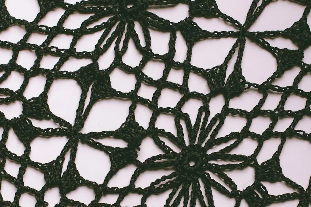 Close-up of black lace fabric with a floral pattern on a pale pink background.