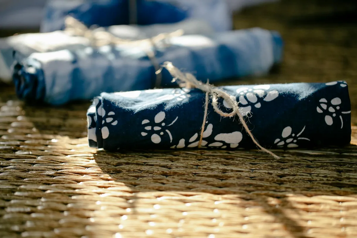 Rolled indigo-blue fabric with a white floral pattern tied with twine, resting on a woven surface