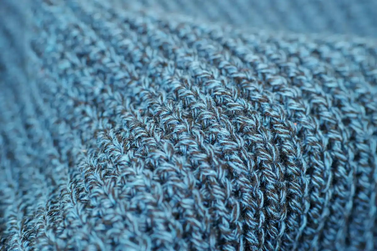 Close-up image of blue knitted fabric showing tight interlocking stitches and textured fiber surface