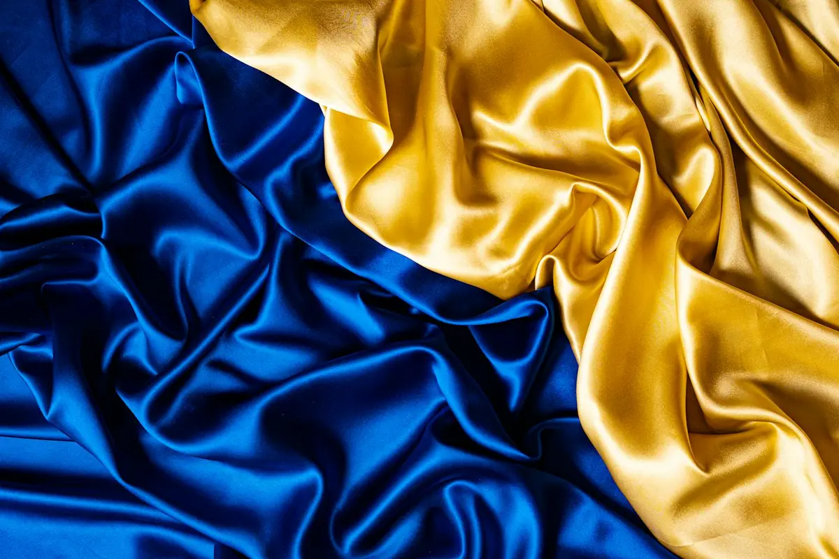 Close-up of blue and gold satin fabric with draped folds and a glossy sheen.