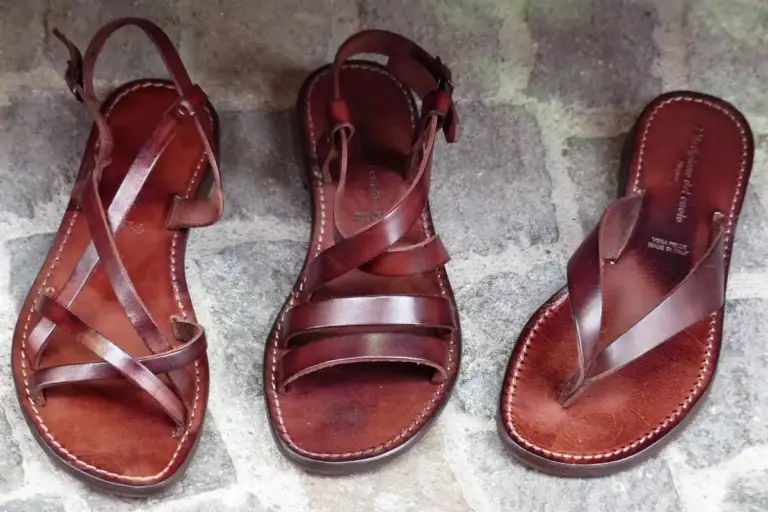 Three brown leather sandals with stitched edges arranged on a stone pavement