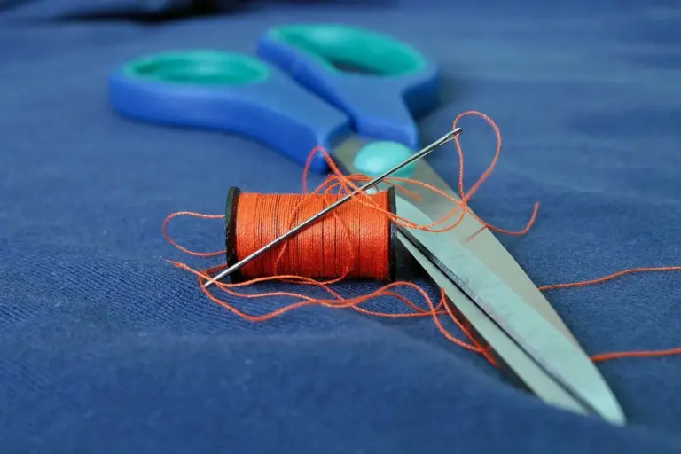 Close-up of blue fabric with a spool of orange thread and blue-handled scissors.