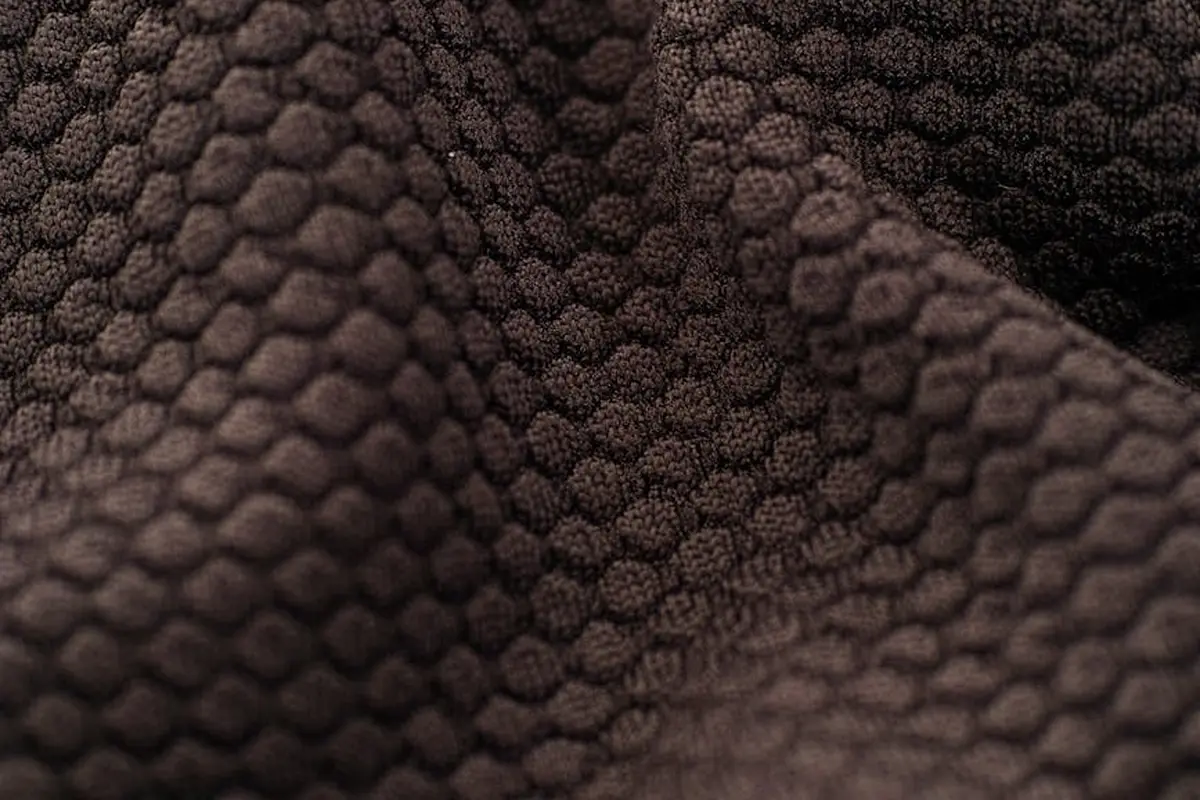 Macro shot of a deep brown fabric with a pebbled, honeycomb-like texture.
