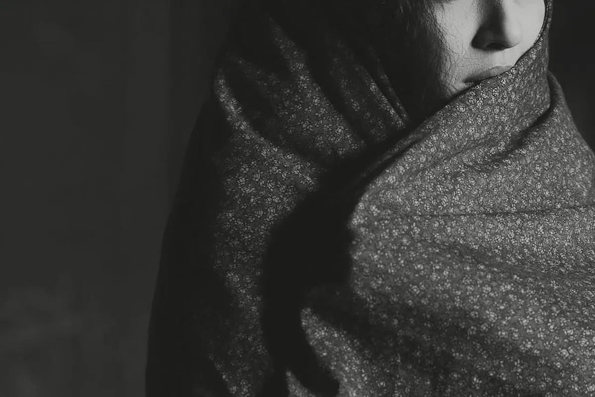 A close-up, black-and-white image of a person wrapped in a patterned scarf, covering part of the face.