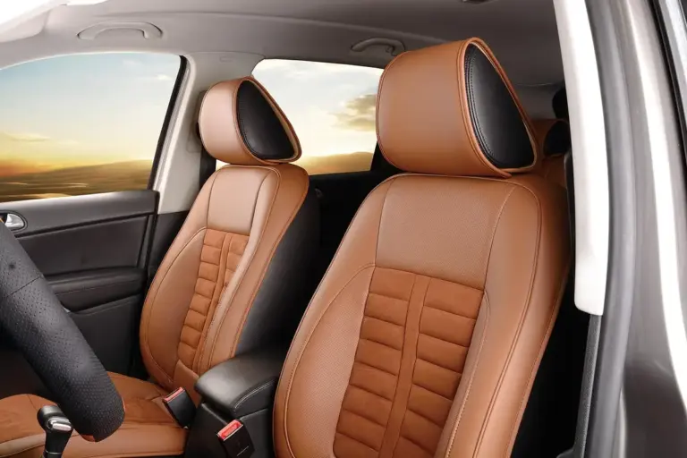 Front seats of a car with tan leather upholstery, showing detailed stitching and headrests with sunlight streaming through the window.