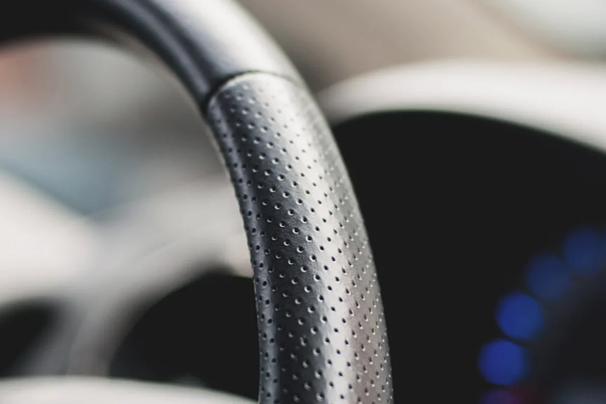 Close-up of a perforated black leather steering wheel with visible stitching and grain texture.