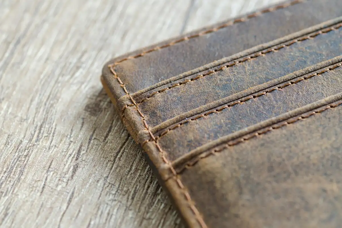 Close-up of brown distressed leather with visible topstitching along the edge, showing texture and patina.