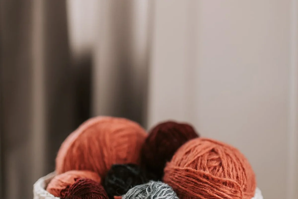 Assorted yarn balls in warm colors (orange, pink, red, gray) sitting in a white bowl