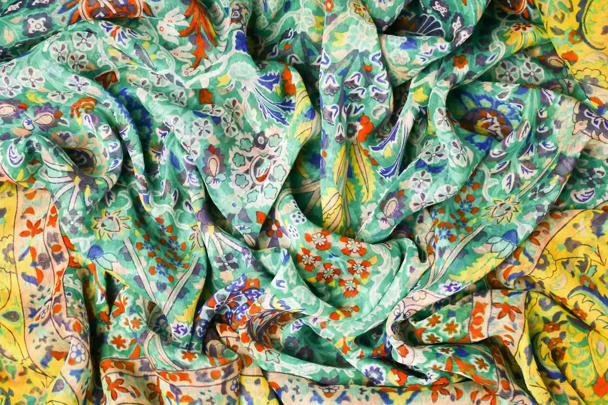 Close-up of crumpled, brightly dyed fabric with teal, green, and yellow floral patterns.