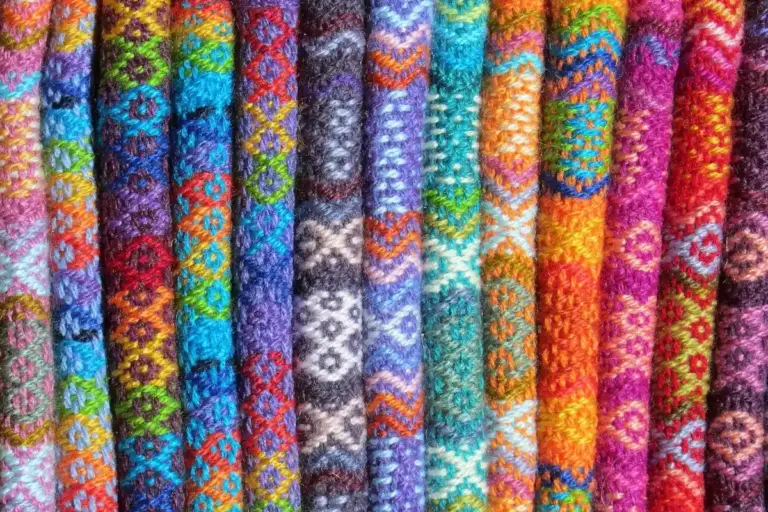 Rows of bright, woven fabric rolls in rainbow colors with geometric patterns.