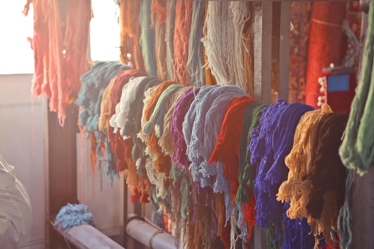 Rainbow-colored skeins of fiber hanging on a rack in a textile workshop.