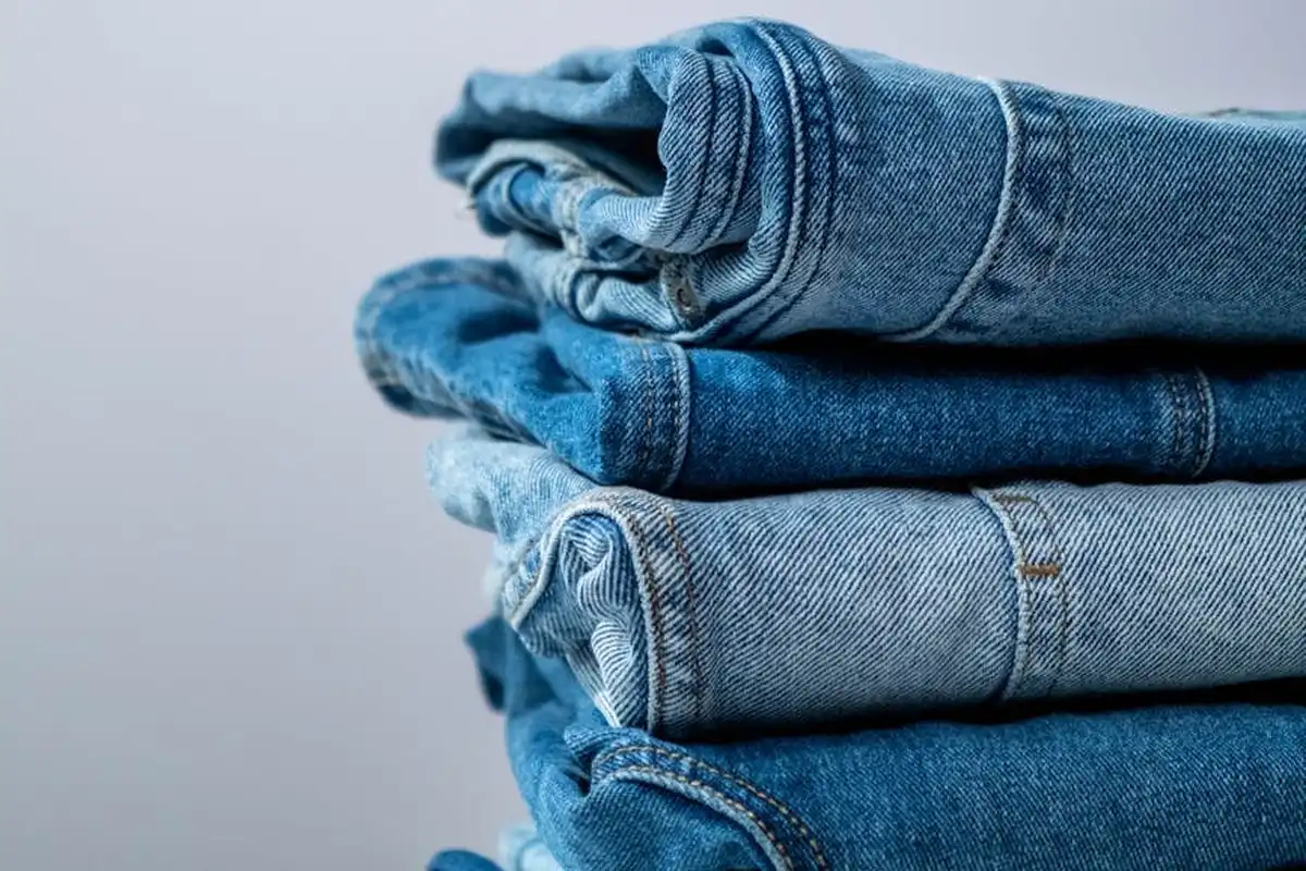Stack of folded denim fabric in varying blue shades, a cotton material ready for cutting and sewing