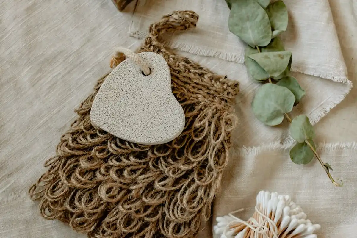 Natural hemp fiber wash scrubber with a tag, resting on light fabric with a sprig of eucalyptus nearby.