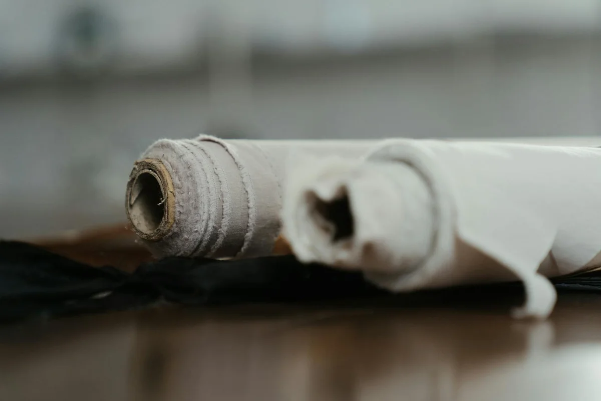 Close-up of rolled fabric samples on a wooden table, showing natural beige fibers typical of unbleached cotton or hemp.