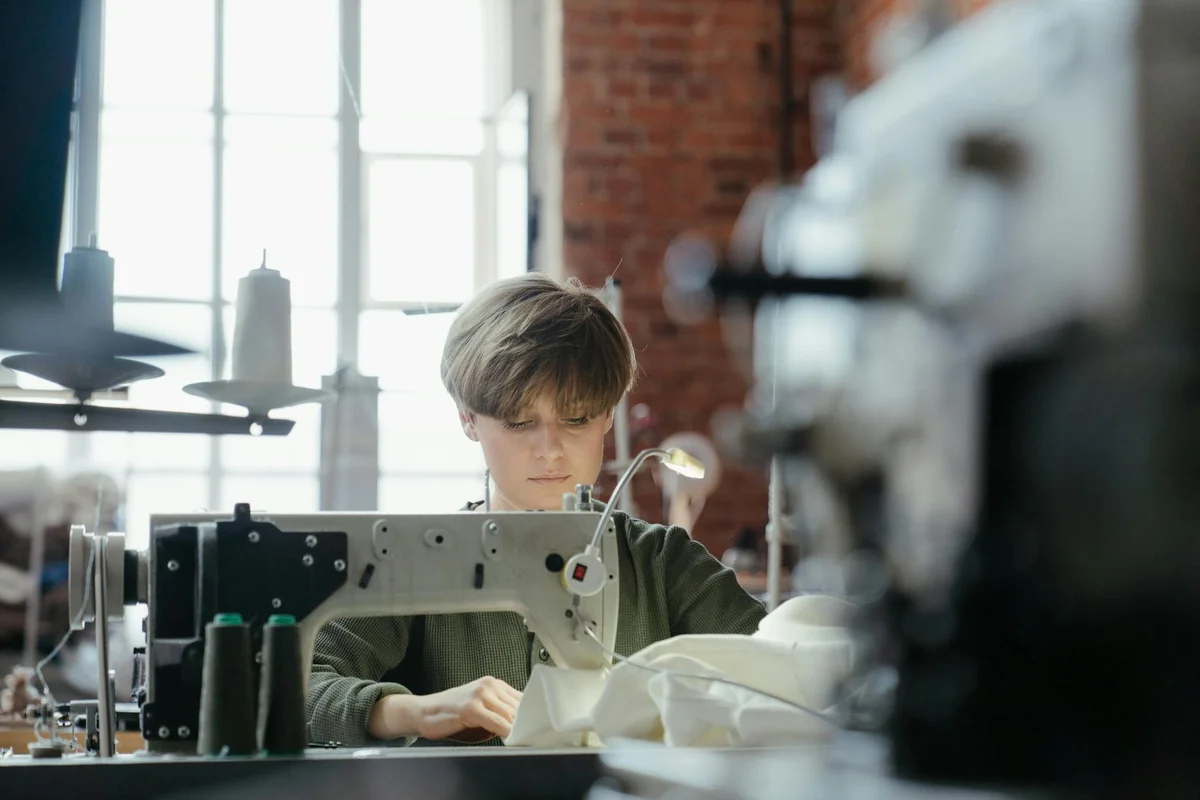 Person operating a sewing machine in a bright workshop, illustrating a hands-on non-destructive approach to fabric verification.