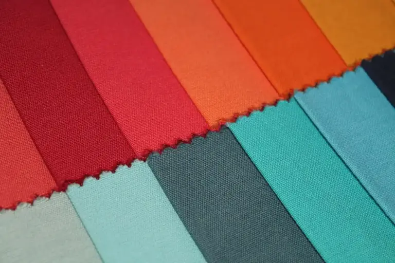 Diagonal arrangement of colorful cotton fabric swatches in red, blue, teal, and gray tones.
