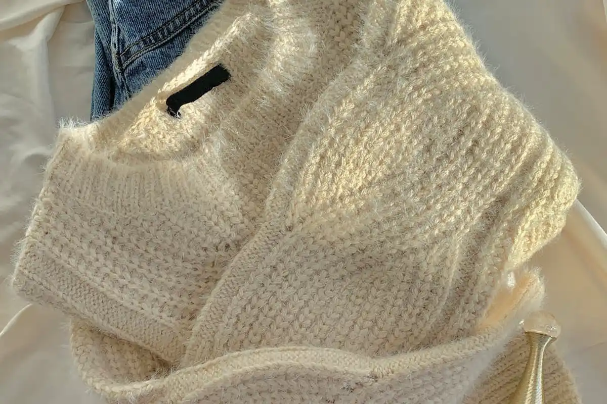 Cream chunky-knit wool garment laid on a white surface, with a piece of denim fabric visible in the corner.