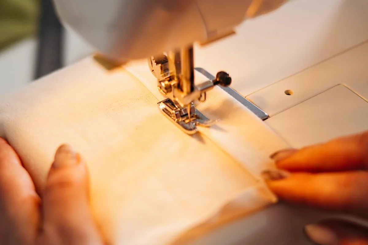 Close-up of a sewing machine sewing a fabric edge, with hands guiding the fabric.