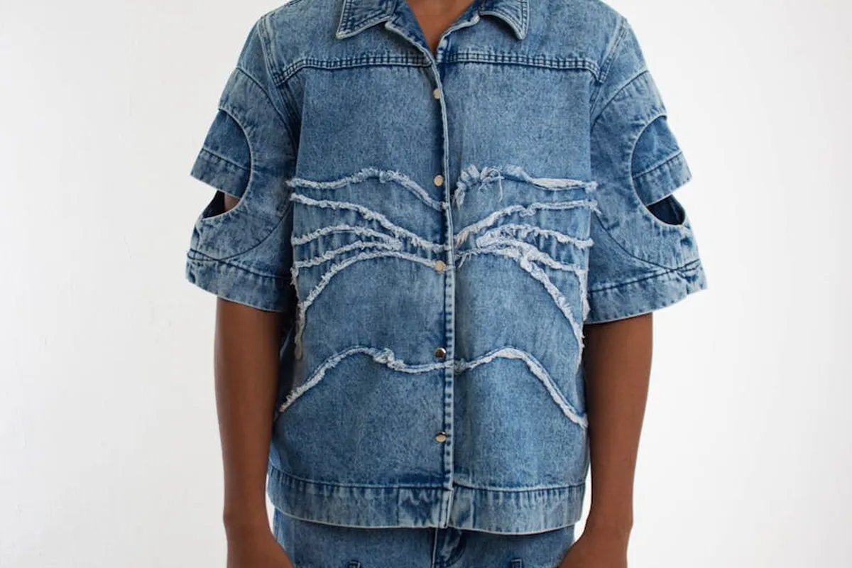 Person wearing a blue denim jacket with ripped panels on the chest and sleeves.