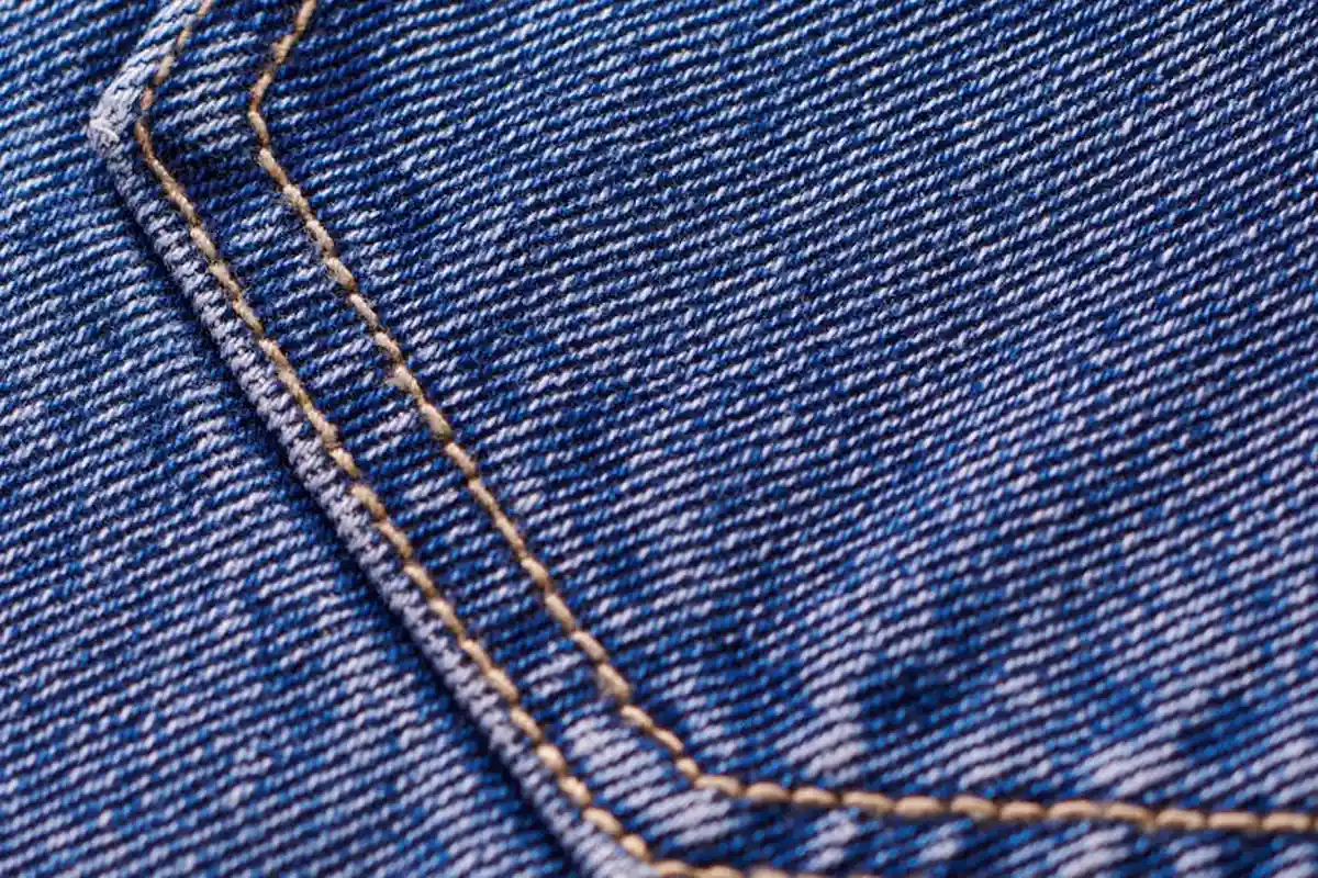 Close-up of blue denim fabric showing diagonal twill weave and orange-brown stitching
