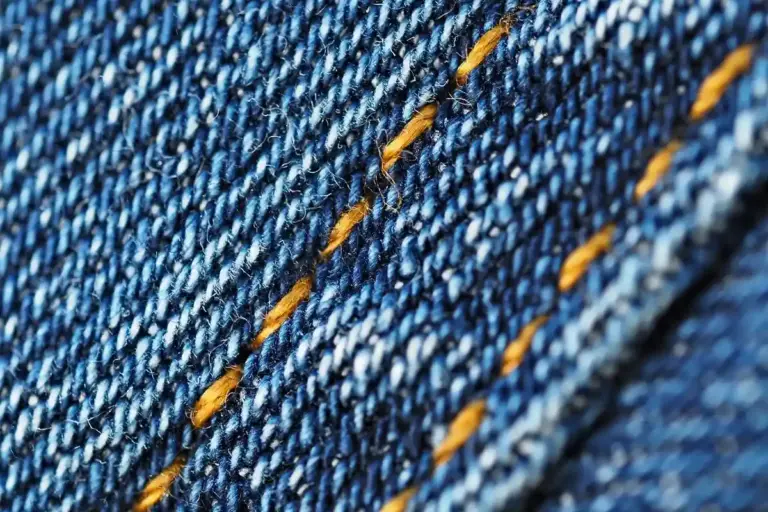 Close-up of blue denim fabric with orange stitching.