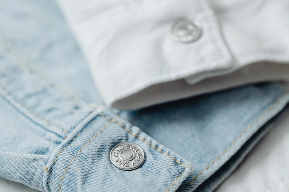 Close-up of light blue denim fabric with a metal button/rivet