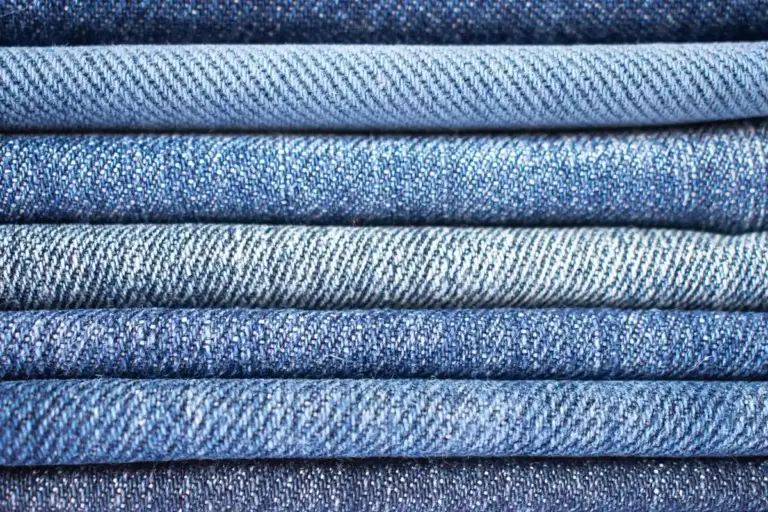 Close-up of folded denim fabric in varying blue tones, highlighting the tight weave texture.