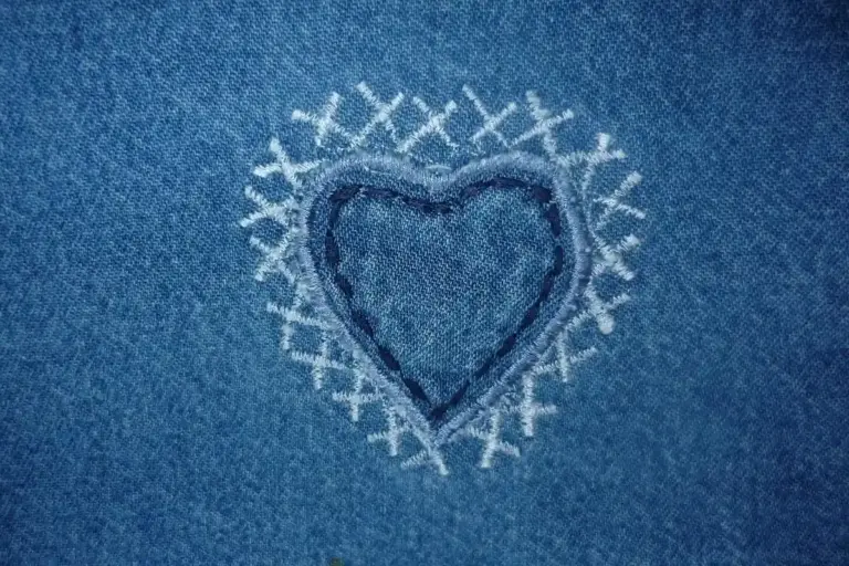 Close-up of blue denim fabric with a white embroidered heart at the center.