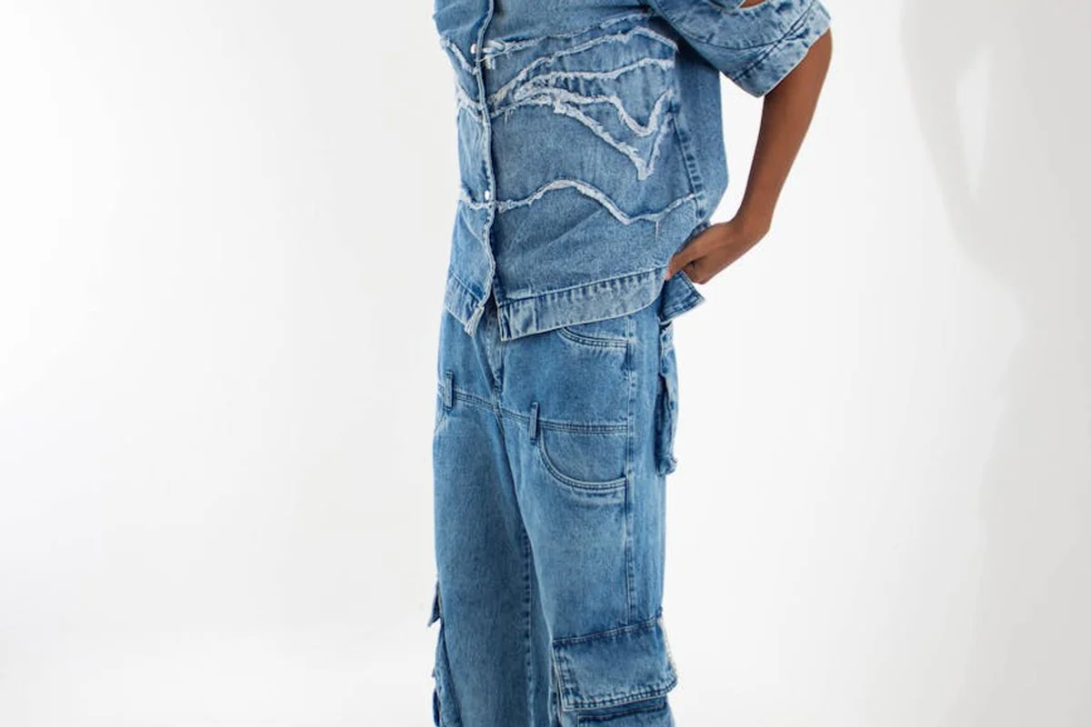 Side view of a person wearing a blue distressed denim patchwork jumpsuit