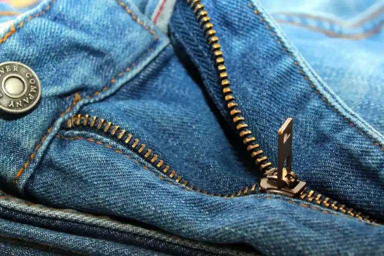Close-up of a brass zipper on blue denim fabric