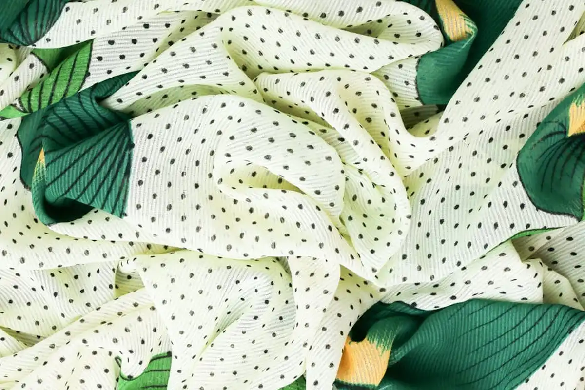 Close-up of white fabric with small black polka dots and green leafy accents.