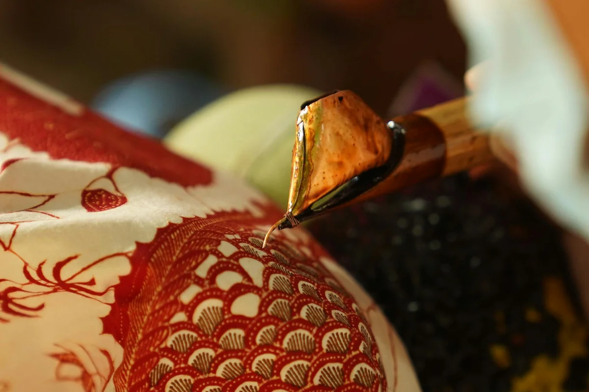 Close-up of a dye brush applying pigment to a textured pile fabric with a red pattern, illustrating corduroy/velvet dyeing.
