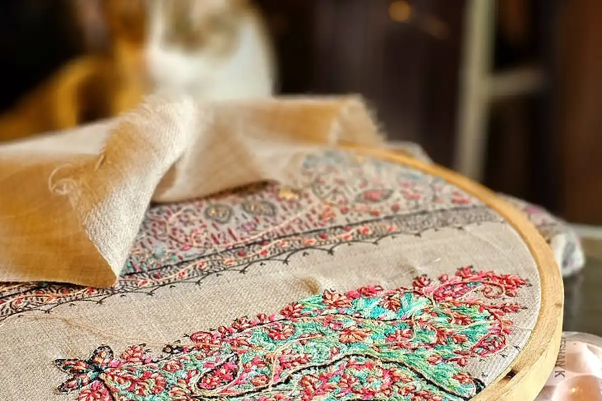 Close-up of a decorative embroidered fabric stretched in a wooden embroidery hoop, displaying colorful floral patterns and textured textile details.