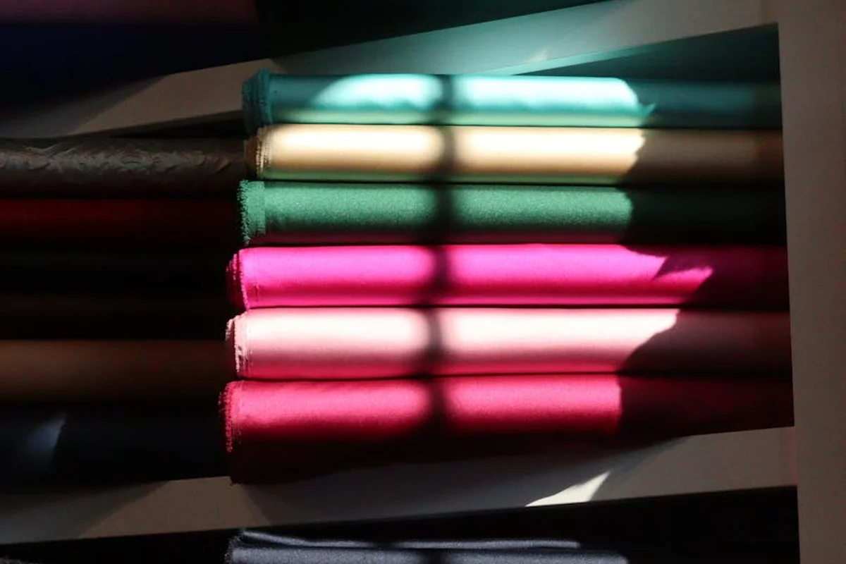 Stacked folded fabrics in teal, green, pink, and other colors, with strong shadows across the folds.