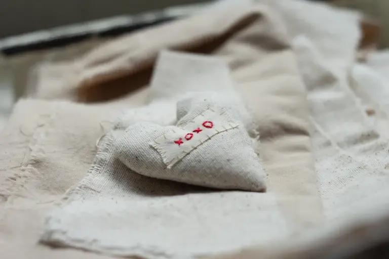 Close-up of light-colored fabric scraps with a small red stitched tag on a soft, textured surface