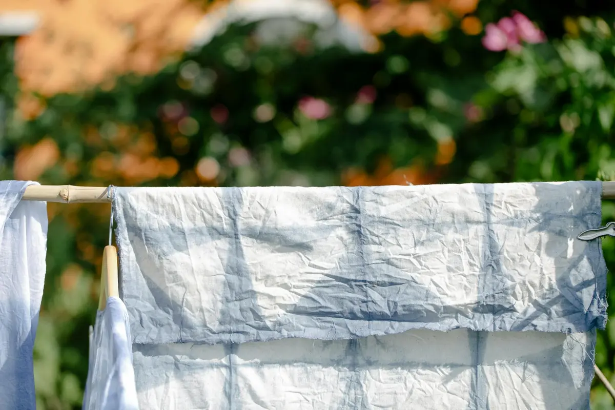 White fabric panels drying on a clothesline outdoors with a blurred garden background