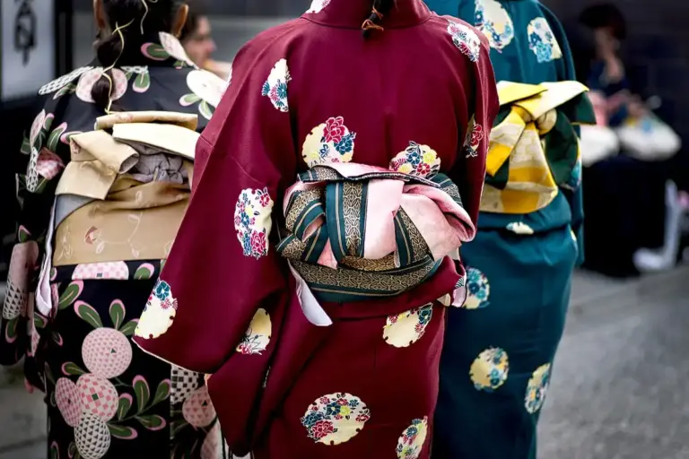 Three people wearing colorful kimonos with obi belts, standing together.
