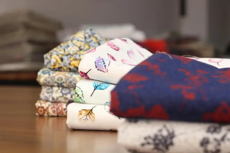 A stack of folded colorful fabrics with floral and geometric patterns on a wooden table