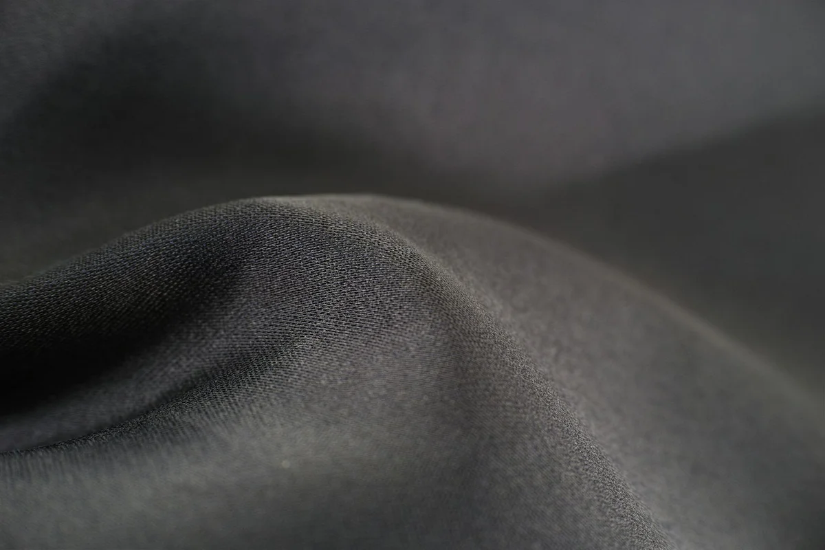 Close-up of dark, smooth fabric with soft folds and a subtle sheen.