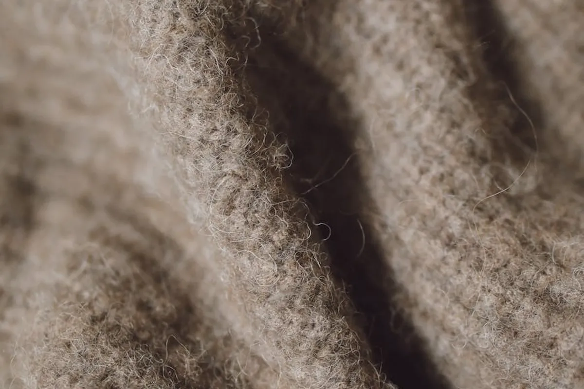 Close-up of fuzzy beige fabric showing wool-like fibers and knit texture.