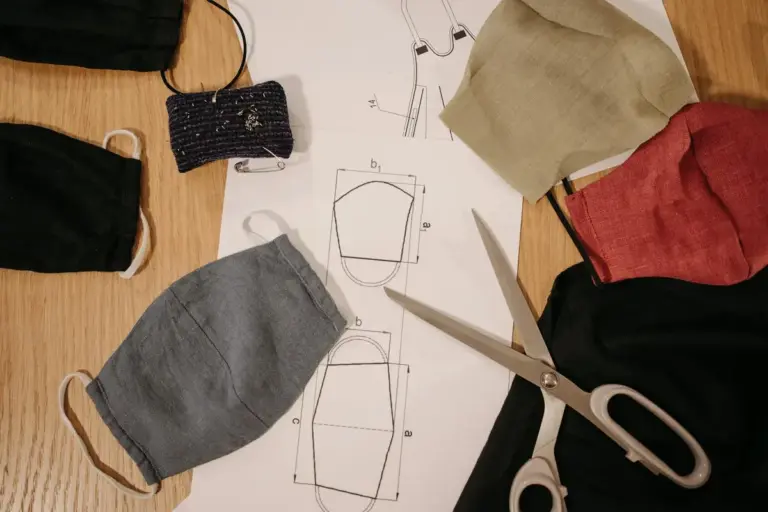 Assorted fabric pieces, a sewing pattern, and scissors laid out on a wooden table for a fabric craft project