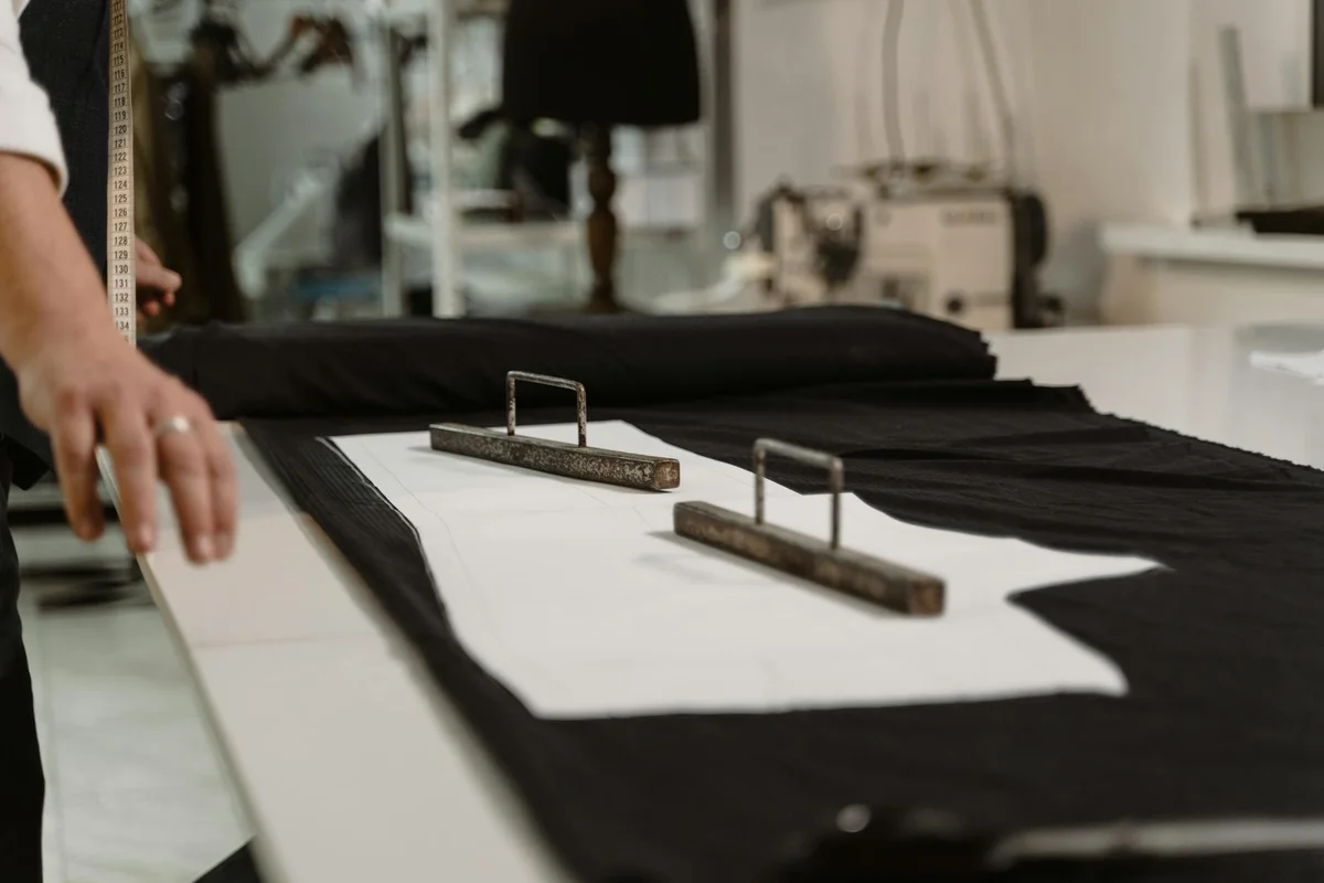 Close-up of black fabric laid out on a cutting table with metal rulers and clamps in a workshop