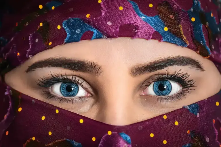 Close-up of a person with bright blue eyes framed by colorful patterned fabric, with a scarf covering the lower part of the face.